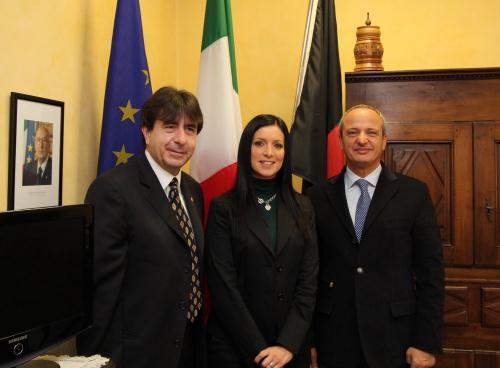 Les Présidents Rini e Pietracupa avec le Viceprésident Lanièce. A l'arriere plan, les symboles de l'autonomie (le drapeau de la Vallée et un produit local) et de la cohésion nationale (le drapeau italien et la photo du Président de la République)